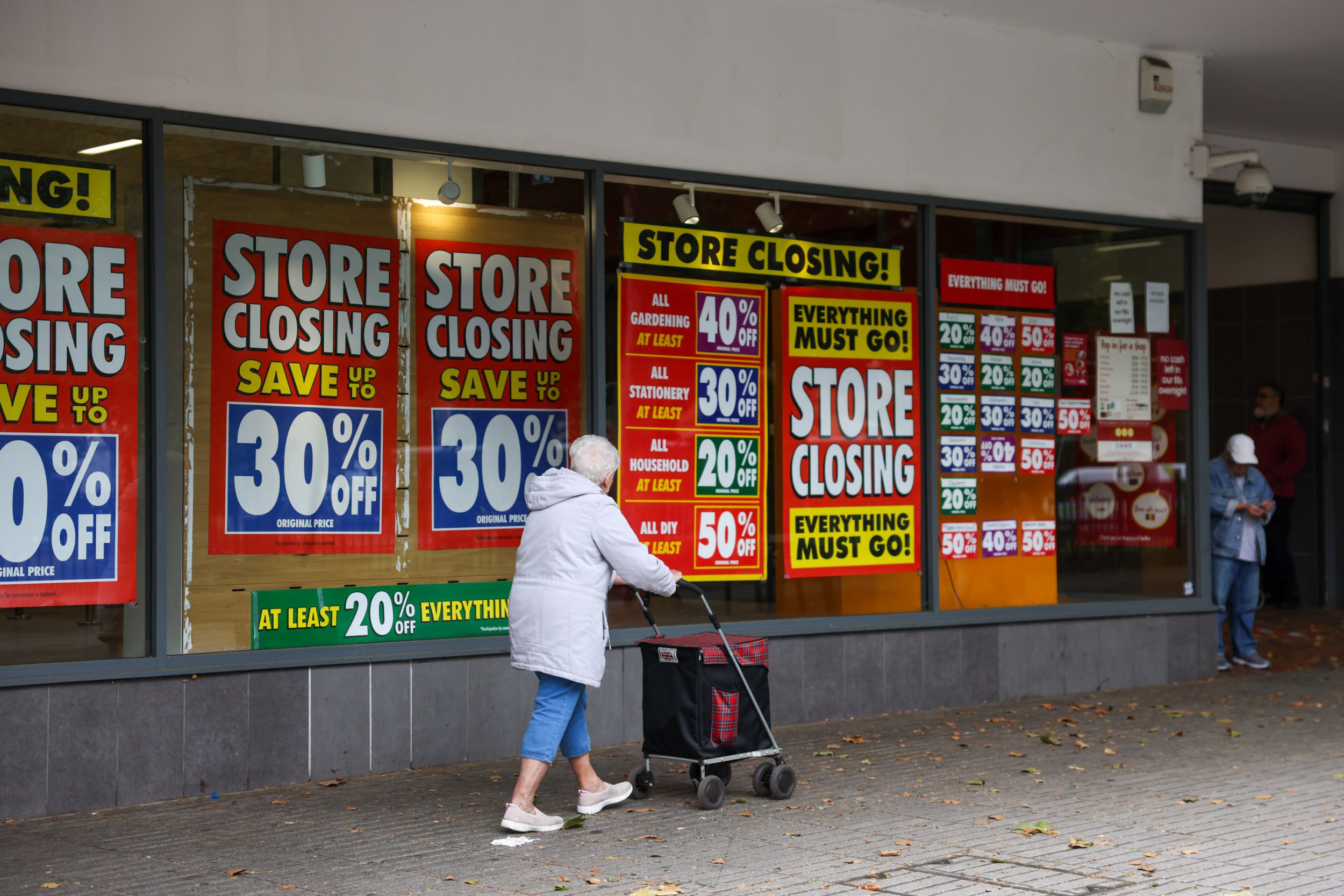 Posters on a window promoting store closing down with a woman walking past.