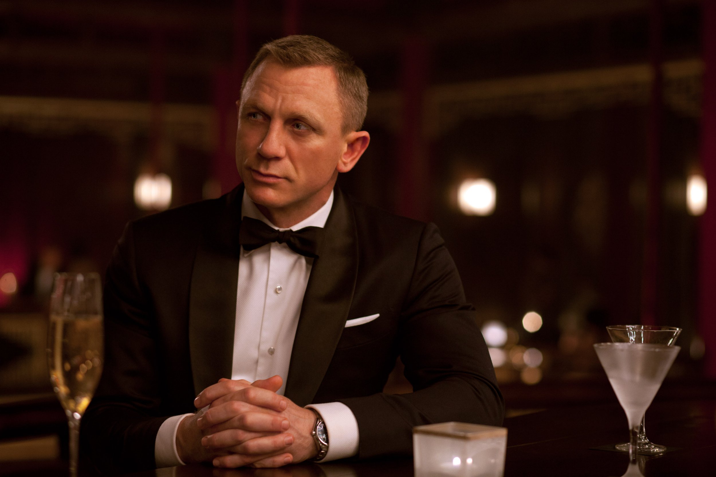 Daniel Craig as James Bond sits at table wearing tuxedo in the movie Skyfall